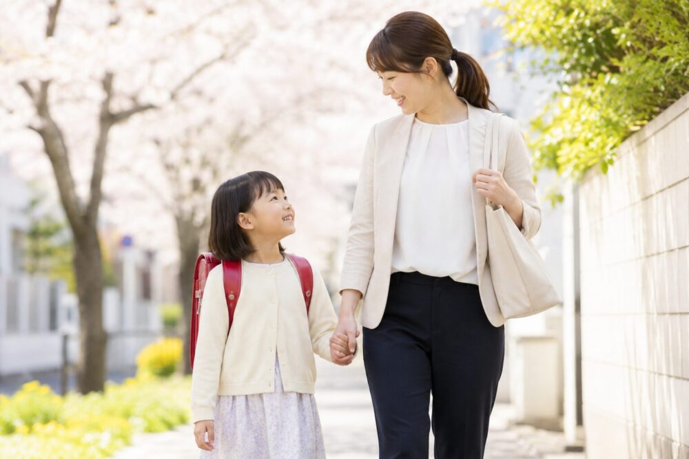 ランドセルを背負って小学校へ向かう子どもと、寄り添う保護者のイラスト